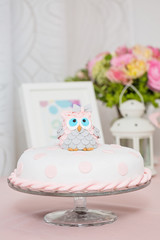 Obraz na płótnie Canvas Birthday cake covered with fondant displayed on the pink cloth and glass tray; decorated with pink dots and an grey and pink fondant owl with blue eyes sitting on top