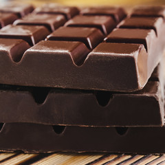 Three pieces of bitter, dark chocolate bar on wooden background, close-up view