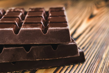 Three pieces of bitter, dark chocolate bar on wooden background, close-up view