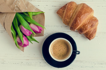 Cup of coffee with bouquet of pink tulips and croissant
