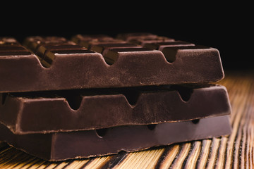 Three pieces of bitter, dark chocolate bar on wooden background, close-up view