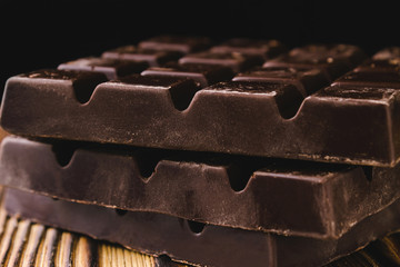 Three pieces of bitter, dark chocolate bar on wooden background, close-up view