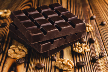 Three pieces of bitter, dark chocolate bar, walnut core and coffee bean on wooden background,...