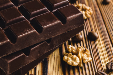 Three pieces of bitter, dark chocolate bar, walnut core and coffee bean on wooden background,...