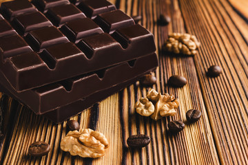 Three pieces of bitter, dark chocolate bar, walnut core and coffee bean on wooden background,...