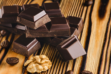 Pieces of bitter, dark chocolate, cubes on heap, walnut core and coffee bean on wooden background, close-up view