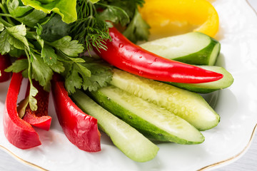 Vegetable slices with cucumber, tomatoes, paprika, lettuce, dill and herbs on white plate. Close up with selective focus