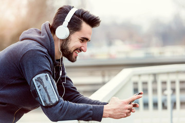 Urban handsome man jogger with earphones taking break listening music