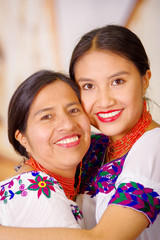 Beautiful portrait of mother with daughter, both wearing traditional andean clothes and matching necklaces, posing embracing happily