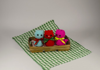 Knitted small red, pink and blue cat on a wicker basket and checkered tablecloth. Handmade. Toy