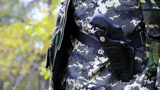 Man in military uniform with revolver in holster. Hunter keeps black revolver in leather holster on the belt