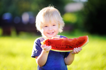 Little boy with blond hairs eating fresh watermelon