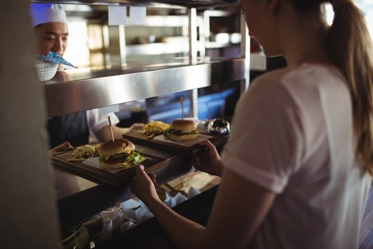 Chef passing tray with French fries and burger to waitress 