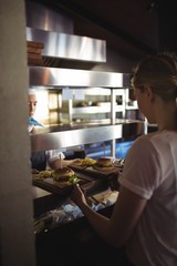 Fototapeta premium Chef passing tray with french fries and burger to waitress 
