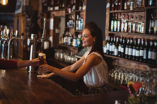 Female bar tender giving glass of beer to customer