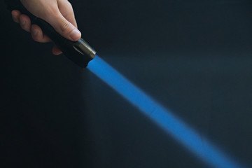 led flashlight with blue beam light in the man's hand from the upper left corner of the frame.
