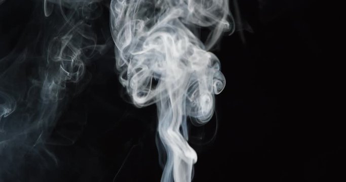 Clouds of white smoke rise into frame in slow motion on black background