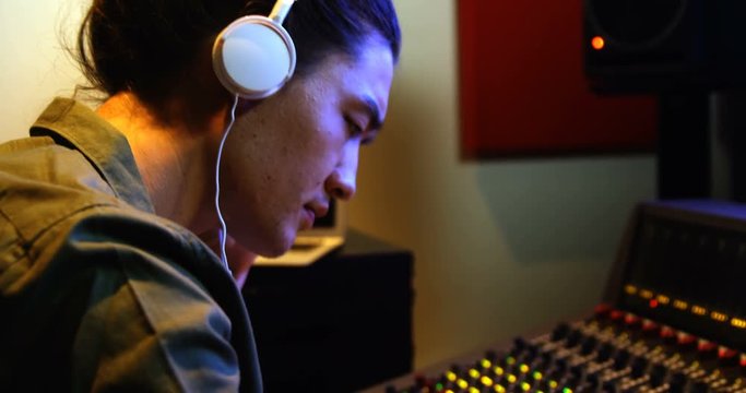 Male audio engineer listening to headphones while mixing sound