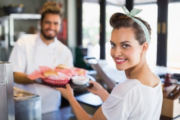 Portrait of waitress taking plate from chef in kitchen
