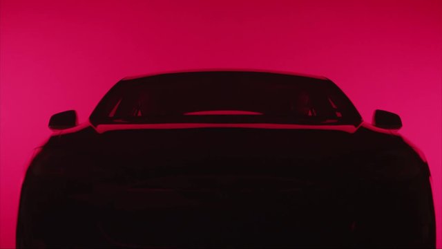 TILT DOWN on silhouette of a sleek car against red background, straight-on shot