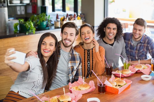 Woman taking selfie with cheerful friends in restaurant
