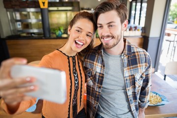 Cheerful friends taking selfie with mobile in restaurant