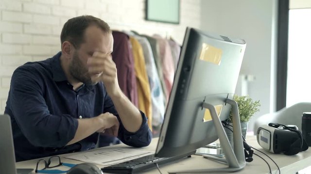 Tired man yawning and falling asleep by table at home
