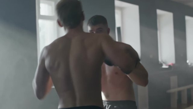 Slow motion shot of shirtless MMA fighter punching his opponent, then performing takedown and being held in arm bar on gym floor 