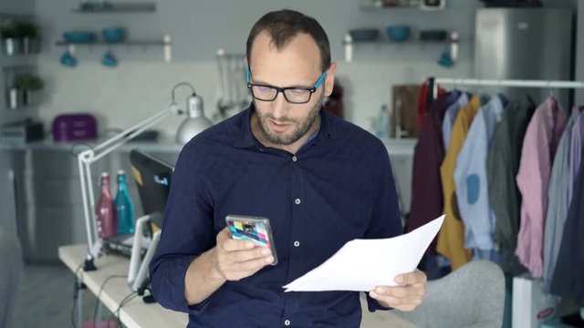 Young man working with smartphone and documents standing at home
