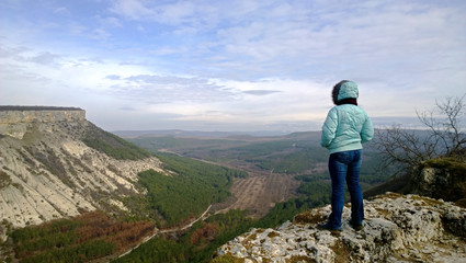 Lonely Mature woman standing on edge of cliff and looks at view. Dressed in a jacket and jeans. The...