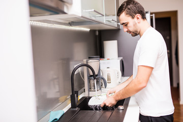 young happy man doing the dishes smiling confident and relaxed enjoying doing domestic work in fun and positive male housework duty