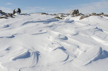 Snow like waves frozen from the winter winds.Blue sky,rocks.