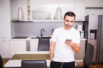 Handsome young man in plaid shirt standing and using smartphone on the kitchen