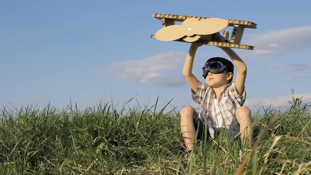 Little boy playing with cardboard toy airplane in the park at the day time. Concept of happy game. Child having fun outdoors. Picture made on the background of blue sky.