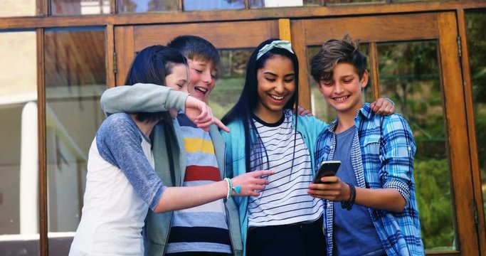 Smiling schoolkids looking photos on mobile phone