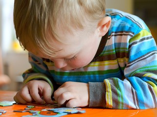 Little boy slouching while playing with puzzle. His wrong way of sitting in chair can influence impairment of posture in future. Child concept © Sasenki