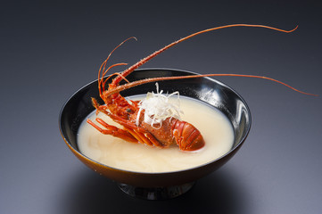 Lobster soup with whole red shrimp in black bowl