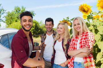 Young people listening guy playing guitar friends drinking beer bottles outdoor countryside, two couple standing near car happy smile summer sunflower