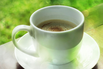 Cup of coffee on wooden table with green bokeh.