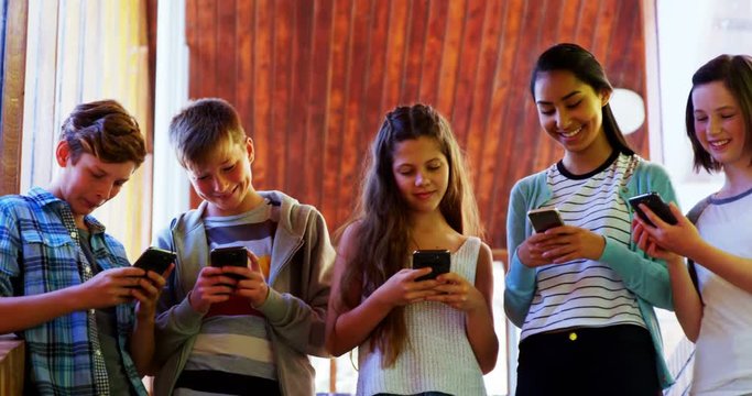 Group of smiling school friends using mobile phone in corridor