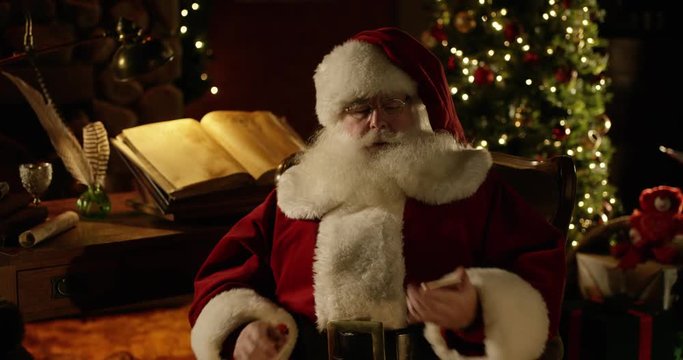 Santa Claus plays with a smartphone in his North Pole workshop
