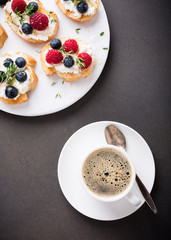 Cup of coffee with berry and goat cheese sandwiches on marble cutting board, top view, copy space.