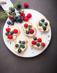 Sandwiches with fresh berries, goat cheese and honey on marble cutting board, top view, copy space.