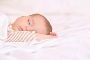 Peaceful baby lying on a bed while sleeping in a bright room