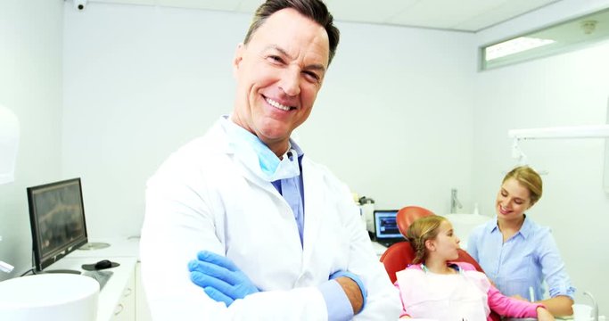Smiling dentist standing with arms crossed at dental clinic