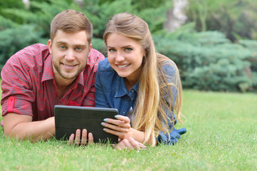 Couple lying in park using tablet pc together on a sunny day