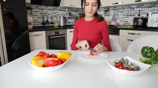 Young beautiful slender woman is cooking. Girl cuts vegetables for salad and smile