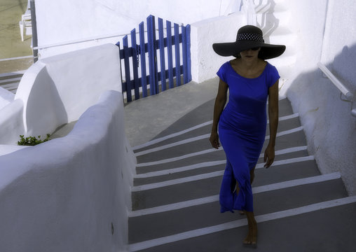 Lady in blue long dress walks on steps in Oia village, Santorini island, Greece