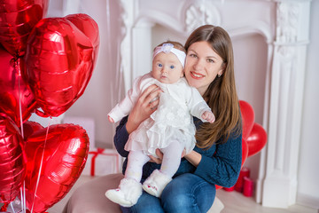 beautiful young mother and daughter in dresses with wreathes on their hads with colorful baloons in photo studio