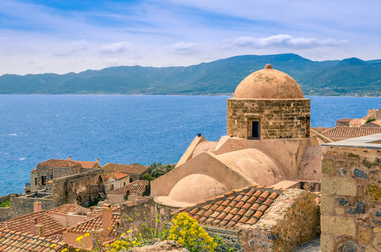 old church surrounded by traditional stone houses inside the castle of Monemvasia overlooking the endless blue of aegean sea.